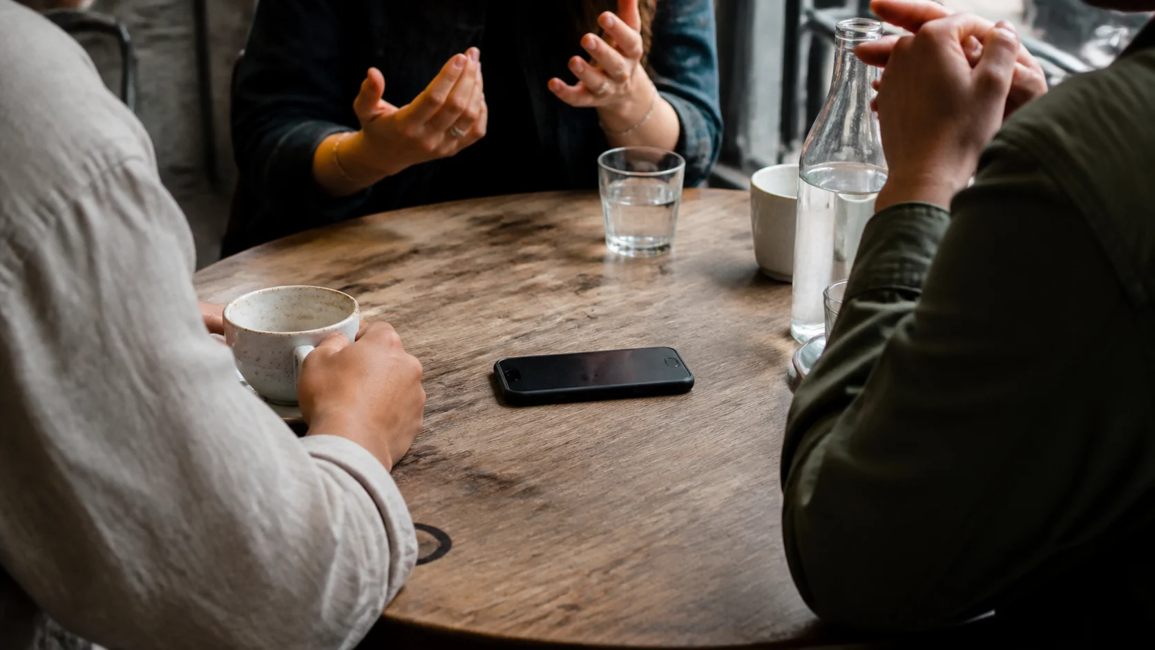 Zwei Menschen im Gespräch an einem Tisch mit Kaffee und Smartphone